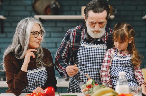 Grandparents and granddaughter preparing salad in home kitchen, creating memories together.